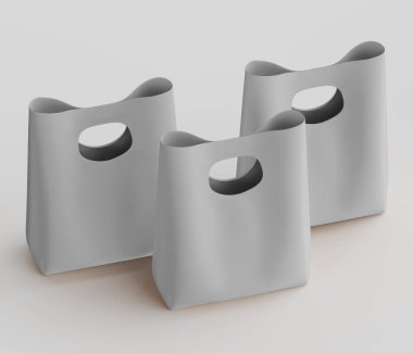 Açık gri, sade ve modern alışveriş torbaları tarafsız bir arkaplanda sergileniyor. Çantaların açık gri bir tonu var. Çantaların oval şekilli sapları pürüzsüz bir dokuya sahip ve hafif sersemletici bir pozisyonda düzenlenmiş. Aydınlık