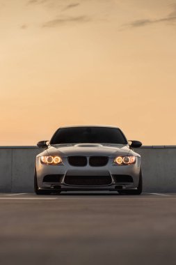 Otoparkta gün batımında arka planı olan güçlü bir arabanın ön görüntüsü.