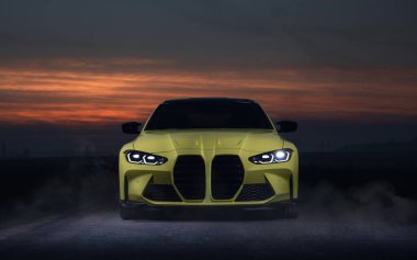 Güçlü sarı spor araba gece yolda, gün batımında arka planda.