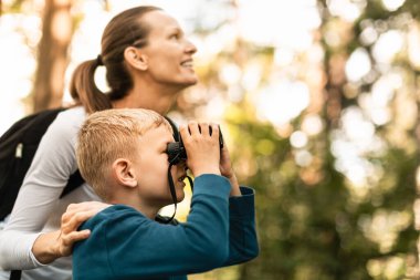 Ormanda dürbünlü bir ebeveyn ve çocuk. Aile doğası keşfi kavramı. Anne ve oğlu ormanı keşfediyor.. 
