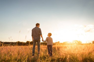 Baba oğul bir yaz tarlasında el ele yürüyorlar, ebeveyn çocuk aile ilişkisi kavramı..