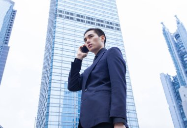 Takım elbiseli genç Asyalı işadamı şehirde cep telefonuyla konuşuyor. 