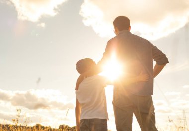 Baba oğul doğada gün batımını izliyorlar, ebeveynlik, aile bağları. 