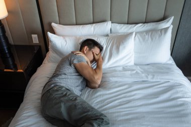 Yatakta yatan uykusuz adam stresli hissediyor.