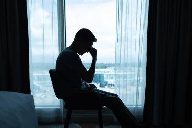 Çaresizlik düşünceleriyle dolu karanlık bir odada üzgün bir adam. Düşünceli üzgün bir adamın portresi. Korku, üzüntü, istismar, depresyon, bağımlılık.