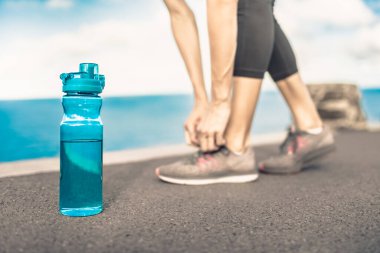 Kadın koşucu ayakkabısını bir şişe içme suyunun yanına bağlıyor.