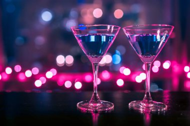 Koyu arkaplanda pembe ve mavi ışıkları olan kokteyl bardakları..