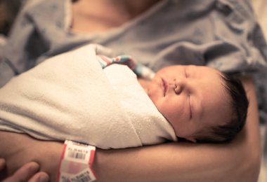 Yeni doğmuş bebek hastanede annesinin kollarında uyuyor. 