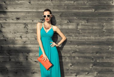 Moda çekimi, elbise giymiş çekici bir kadın, güneş gözlüğü, el çantası. Moda modeli.  