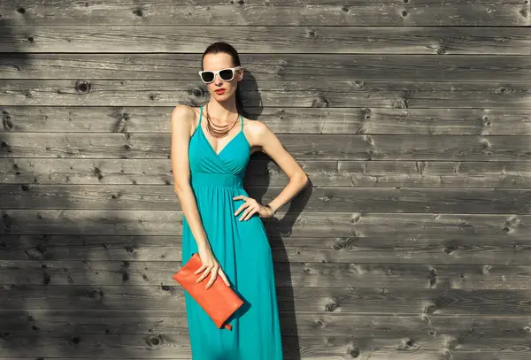 Moda çekimi, elbise giymiş çekici bir kadın, güneş gözlüğü, el çantası. Moda modeli.  