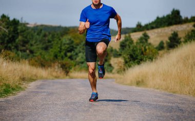 muscular male runner running on asphalt road in field