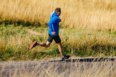 male runner running on road among dry grass