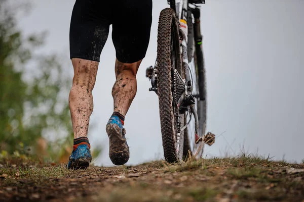 athlete goes uphill with his mountain bike. drops dirt on feet and bike. cross-country cycling competition