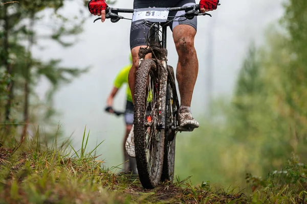 マウンテンバイクのアスリートサイクリストは森の正面ビューで上り坂に乗る 泥で足を落とす クロスカントリー自転車競技会 — ストック写真