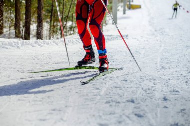 Kayak yarışmasında yokuş yukarı koşan kayakçı, Fischer yarış kayakları, Rossignol kayak botları, bacaklarda HuTag frid etiketi, kış olimpiyatları