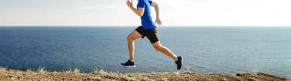 male runner running along seashore trail with dry grass on blue sky background, cross-country running race