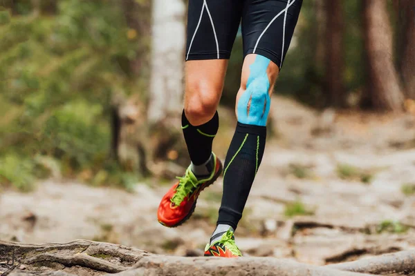Diz üstünde Kinesio bandıyla koşan erkek koşucu orman maratonu, siyah sıkıştırma çorapları ve mavi kinesiotaping.
