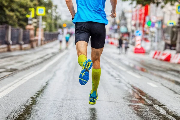 back male athlete in compression socks running marathon in city, summer sports race, jogging on wet asphalt after rain