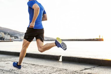 back male runner running embankment in sunrise, jogging along pier in background rising sun and lighthouse clipart