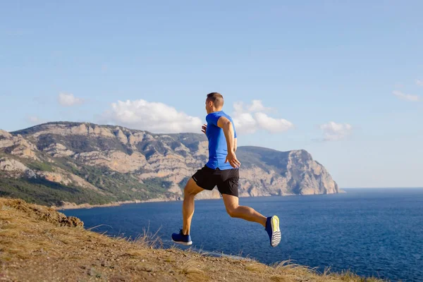海岸沿いの山道やスポーツウェアブルーのシャツと黒のショートパンツ海岸沿いの夏のジョギング — ストック写真
