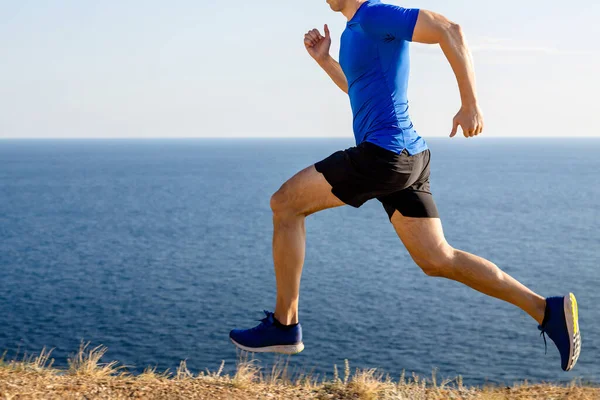 male runner running mountain trail in background of sea and sky, summer jogging along coast