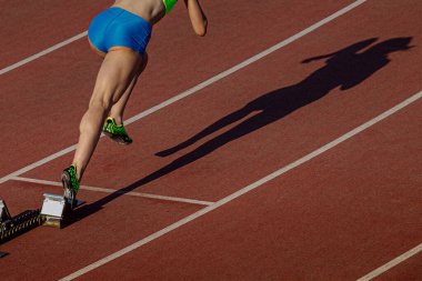 Başlangıç bloklarından başlayan bayan atlet sprint mesafesi, stadyum pistinde gölge kadın koşucu