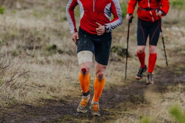 two runners run muddy trail sports race, knee is covered in blood injury from fall clipart