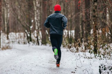 Geri koşan erkek koşucu maraton koşuyor, kış kıyafetleriyle karlı ormanda koşan adam, soğuk hava