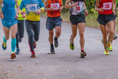 Küçük grup atletleri parkta yolda koşuyorlar, sonbahar maratonu, yere düşmüş sarı yapraklar.