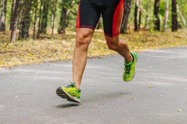 Şehir parkında yolda koşan erkek koşucu, sonbahar maratonu, yere düşen sarı yapraklar.