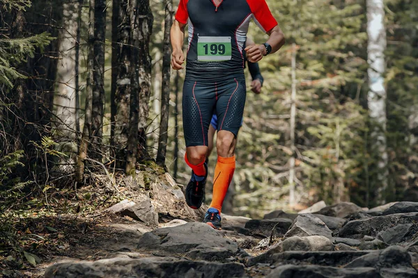 male runner in compression socks running forest trail over stones, summer marathon race