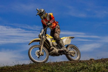 Motokros sürücüsü off-road motor sporu sürüyor arka planda tozlu yarış izleri mavi gökyüzünde