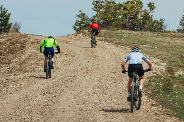 リアビュー3台のマウンテンバイクが上り砂利道で自転車競技会 — ストック写真