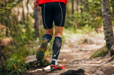 Erkek koşucu Cep kompresyon kolları ve Saucony koşu ayakkabılarıyla orman koşusu maratonu yapıyor.
