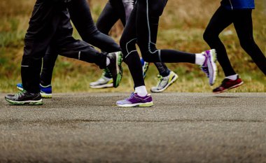 Bacak grubu koşucuları taytlı kadın ve erkekler asfalt yolda bahar yarışı koşuyor.