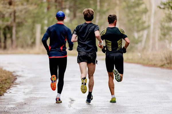 リアビュー3人の男性ランナーが水溜りと水と汚れで道路を走り — ストック写真