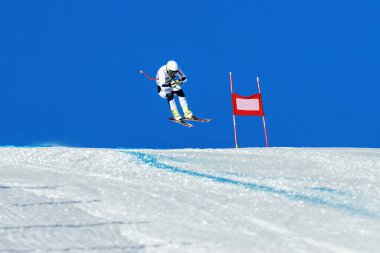 Alp disiplini kayak pistinde kayak yapan erkek kayakçı yokuş aşağı atlar ve tepede uçar.
