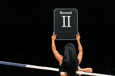brunette ring girl demonstrate sign with number round 2 during fight MMA on dark background clipart