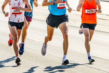 Şehir yolunda maraton koşan dört atlet, tişörtlerde rakamlar, yaz sporları oyunları