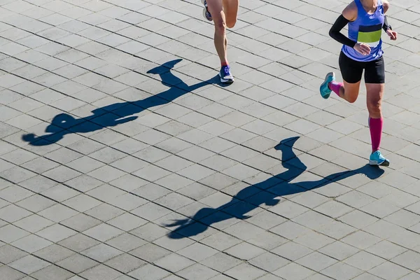 オーバービューマラソンを走る2人の女性選手舗装されたスラブ上のランナーの影 — ストック写真