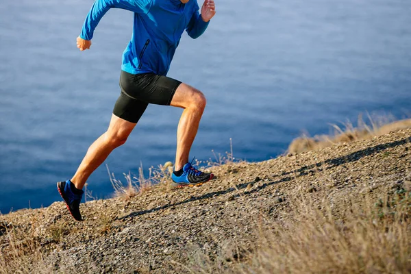 athlete runner start running mountain uphill in blue jacket and black tights, background of sea