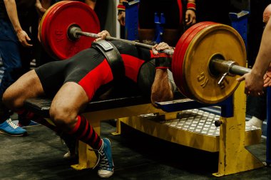 Sporcu, ağırlık kaldırma yarışmasında asistanlarla birlikte göğüs presi yapıyor.