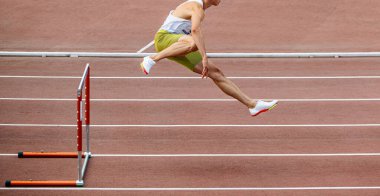 Erkek sporcu yaz atletizm maçlarında 400 metre engelli koşuyor.