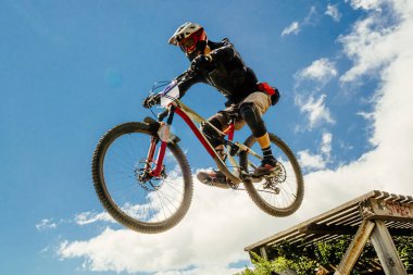 Sporcu bisikletçi uçuşta yokuş aşağı atladı. mavi gökyüzünün arka planına karşı