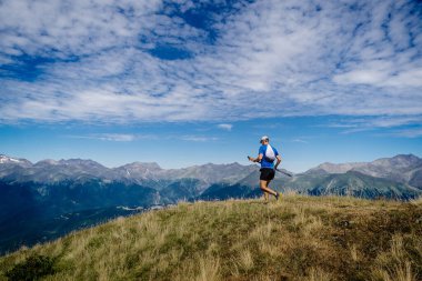 Elinde sırıkla dağ maratonu yapan bir adam.