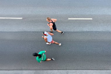 Asfalt yolda koşan üç sporcu, tepeden aşağı manzara