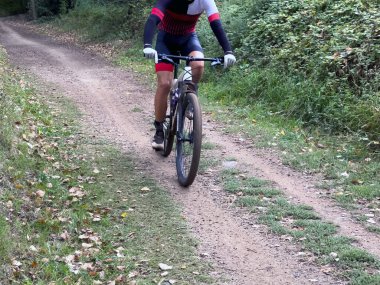 Öndeki adam ormanda dağ bisikleti sürüyor.