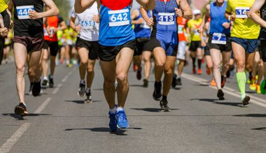 Güneşli bir günde koşucular canlı kıyafetler ve görünür yarış önlükleriyle maratonda yarışıyorlar.