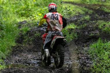 Arka manzara dayanıklı arazi motosikleti sürücüsü bir off-road rac sırasında çamurlu orman patikasında hızla ilerliyor.