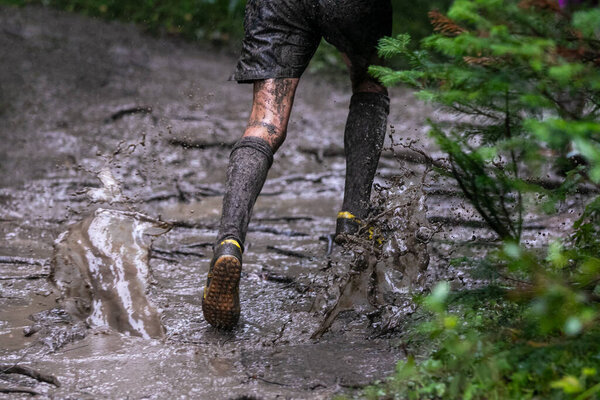 Ноги спортсмена бегают лужи грязи под проливным дождем во время лесного марафона